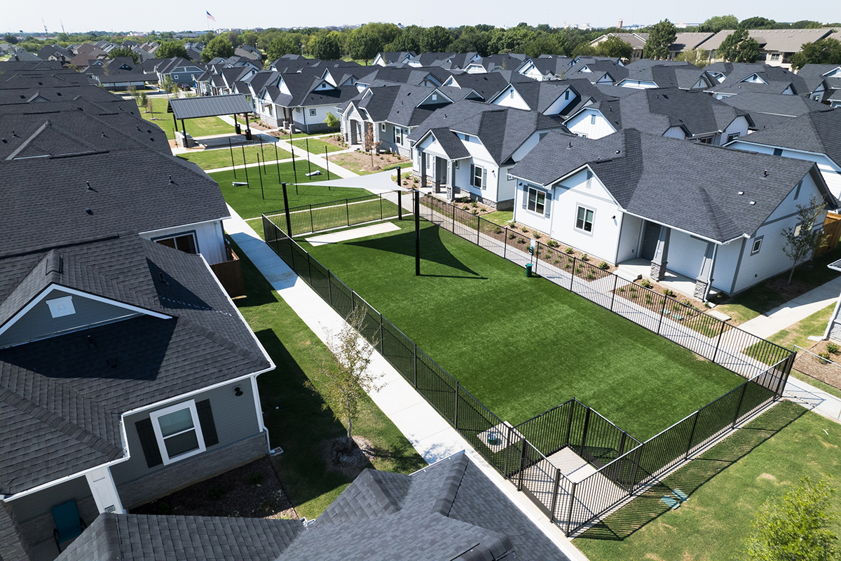 Single family for rent community with white and gray homes facing a dog park with green turf.