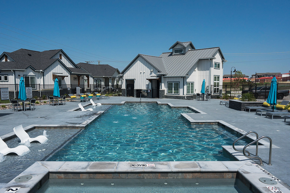 Leasing office with resort-style pool surrounded by gray concrete, pool chairs, and umbrellas.