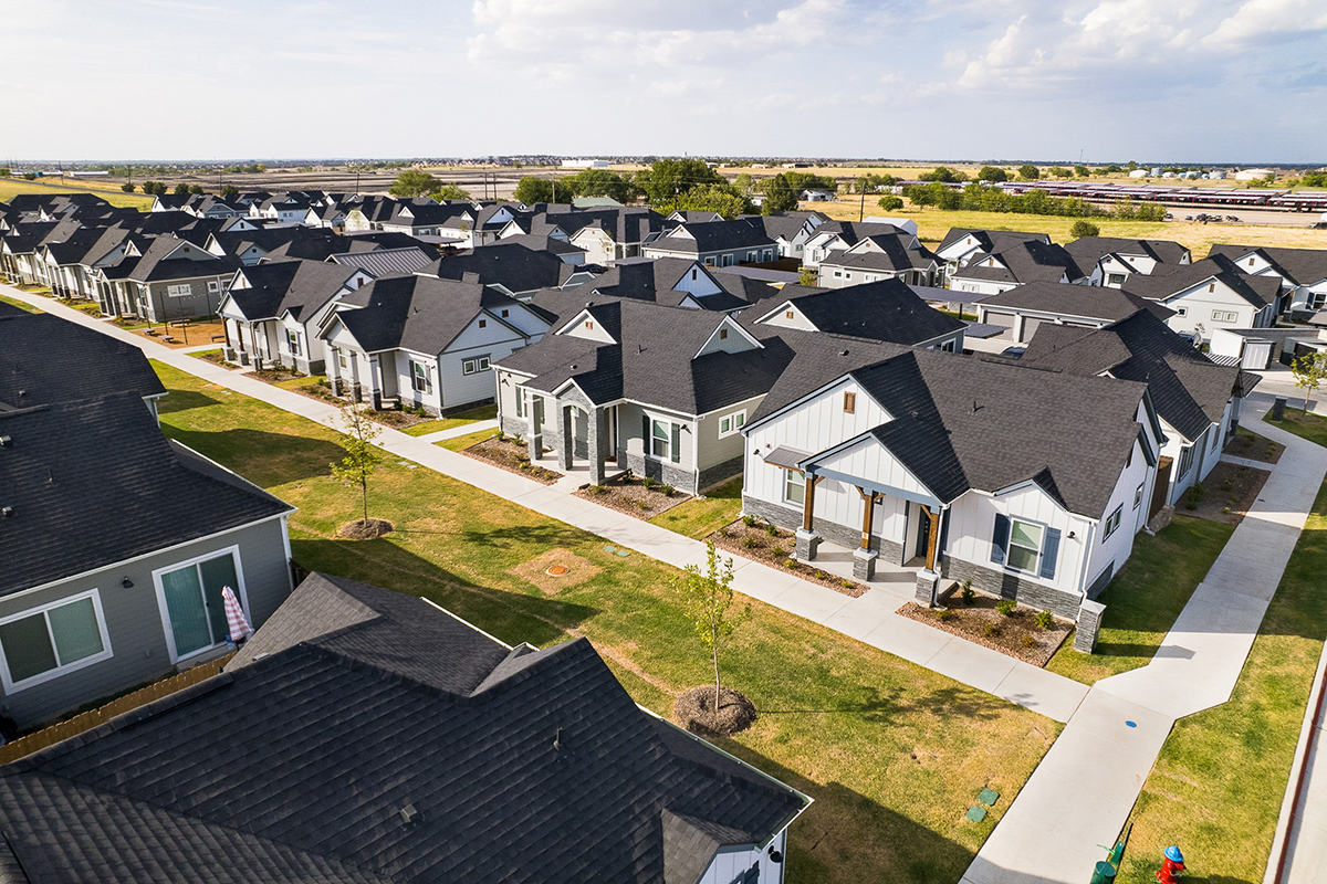 Single family for rent community with gray-colored homes and fenced-in backyards surrounded by green field.