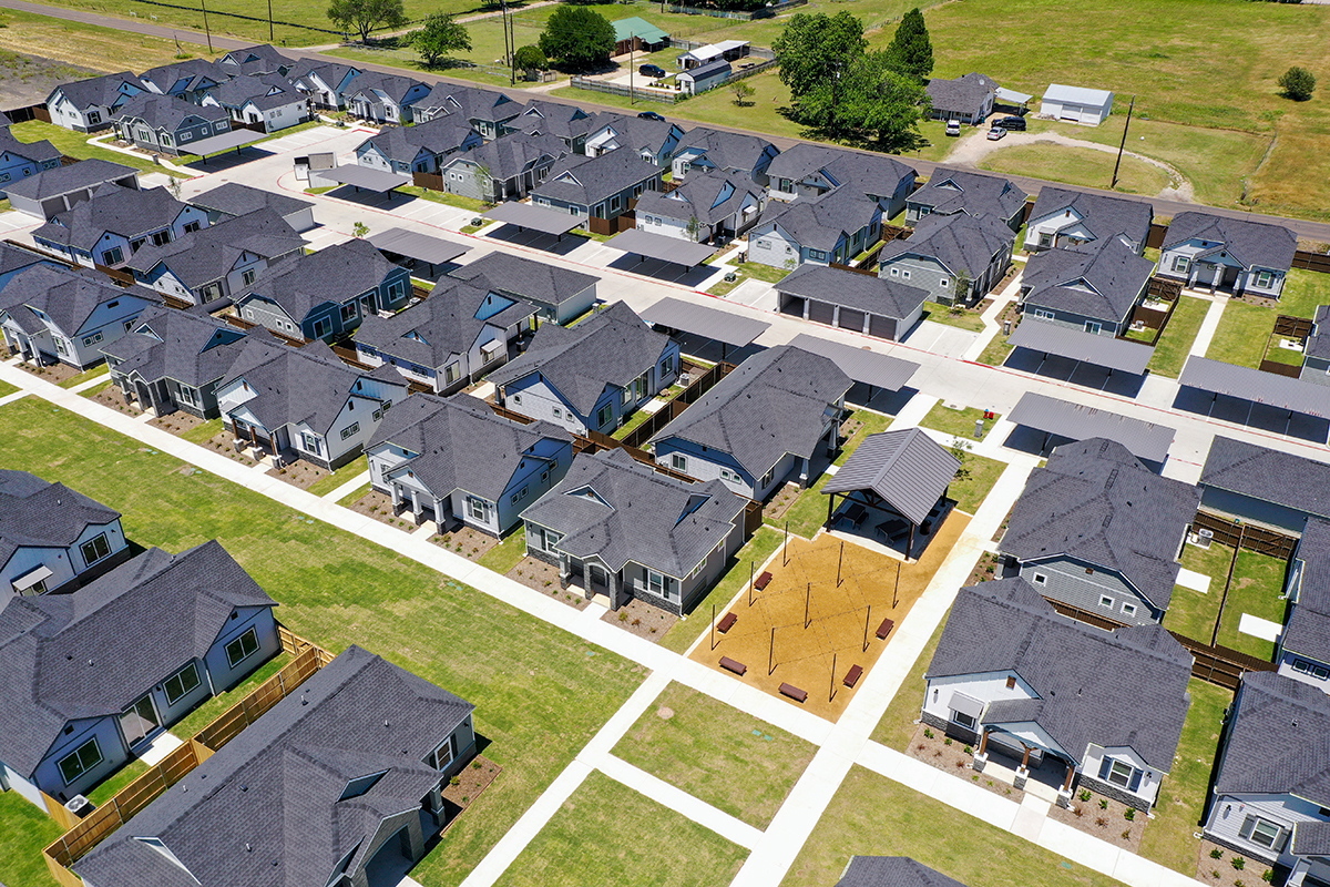 Single family for rent community with gray-colored homes and fenced-in backyards surrounded by green field.