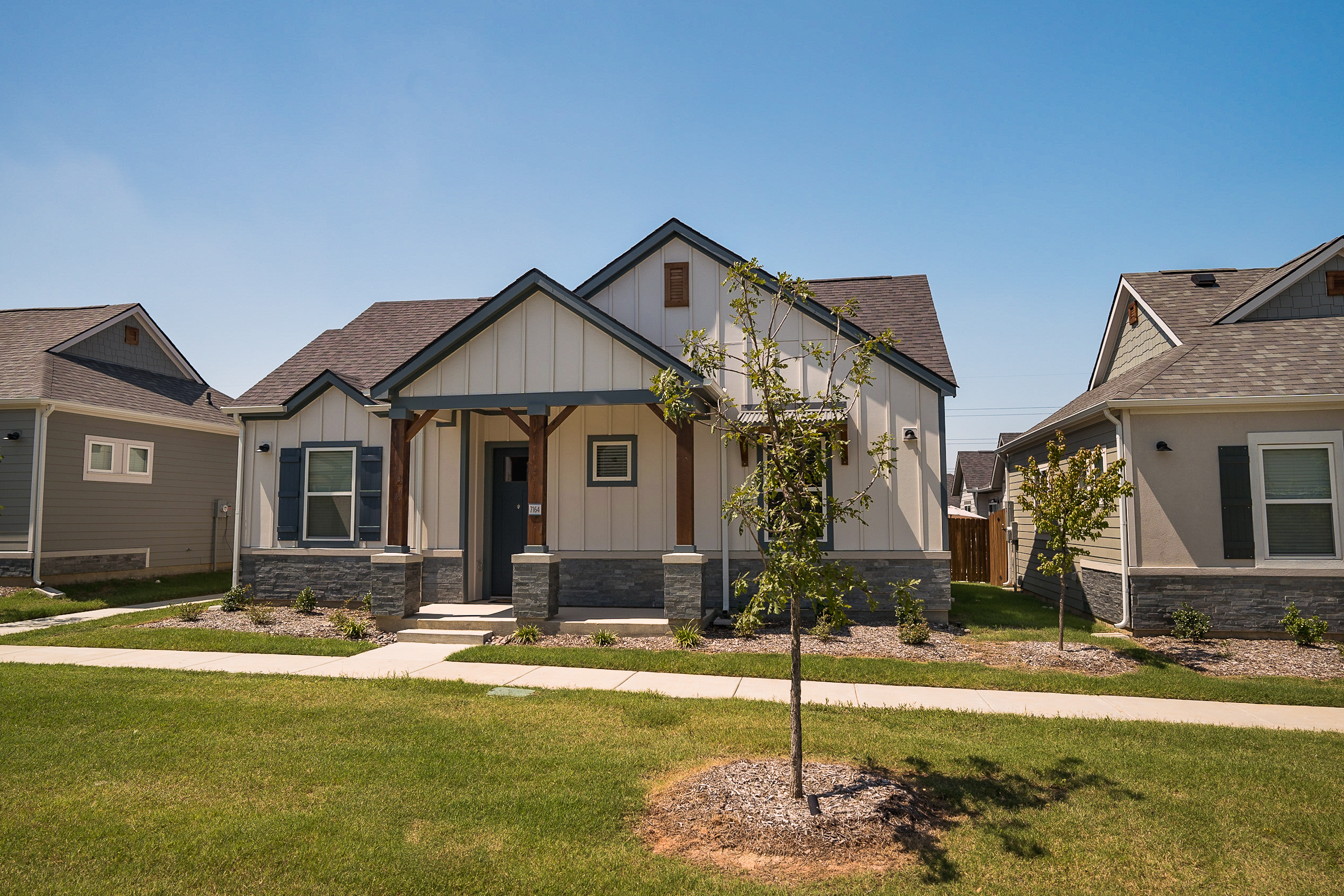 A white and gray single-family home for rent with outdoor greenery and trees.