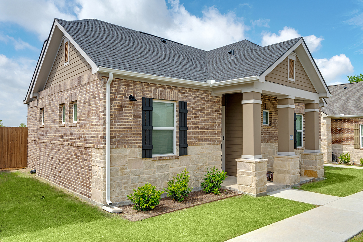 Single family for rent home made of brick and stone with landscaping and green grass.