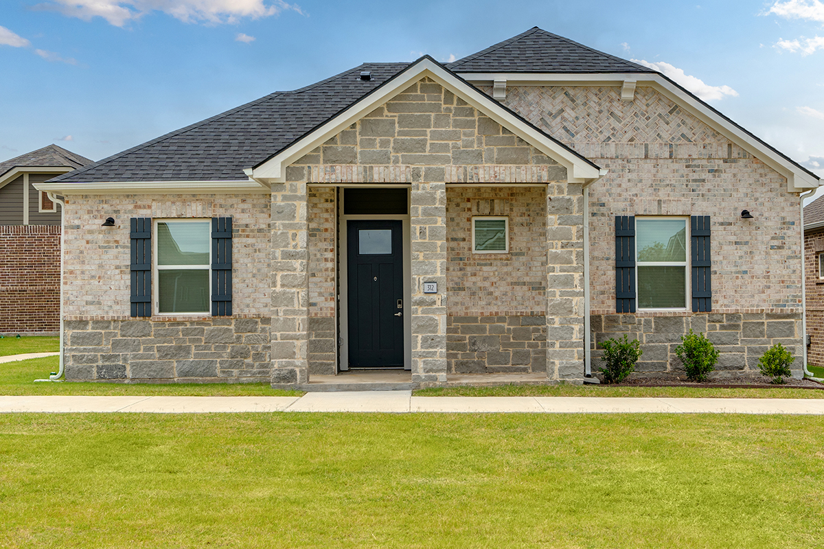 Single family for rent home made of brick and stone with landscaping and green grass.