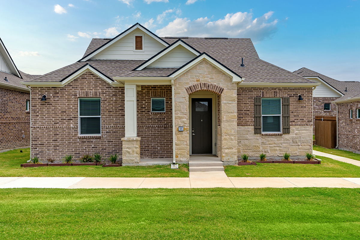 Single family home made of brick and stone with landscaping and green grass.