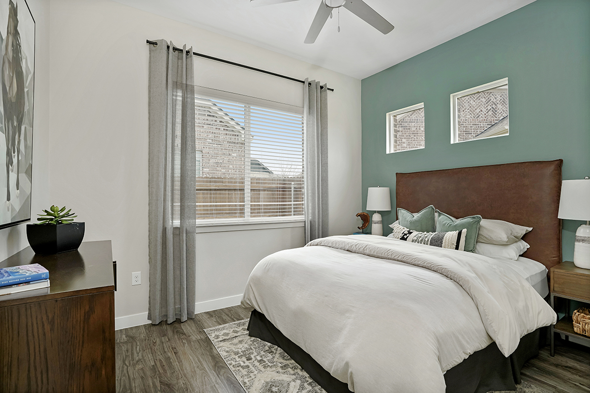 Modern bedroom with a large bed, green accent wall, two nightstands with lamps, a dresser, and a window with gray curtains letting in natural light.