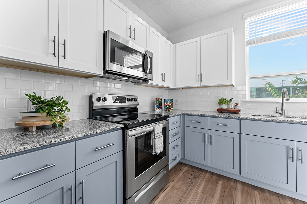 Modern kitchen with white upper cabinets, light blue lower cabinets, stainless steel appliances, a granite countertop, white subway tile backsplash, and a window letting in natural light.