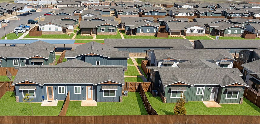 a new build to rent neighbor hood with blue and green siding and brown fencing separating all of the houses