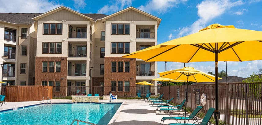 a pool umbrellas and lounging chairs outside of an apartment complex